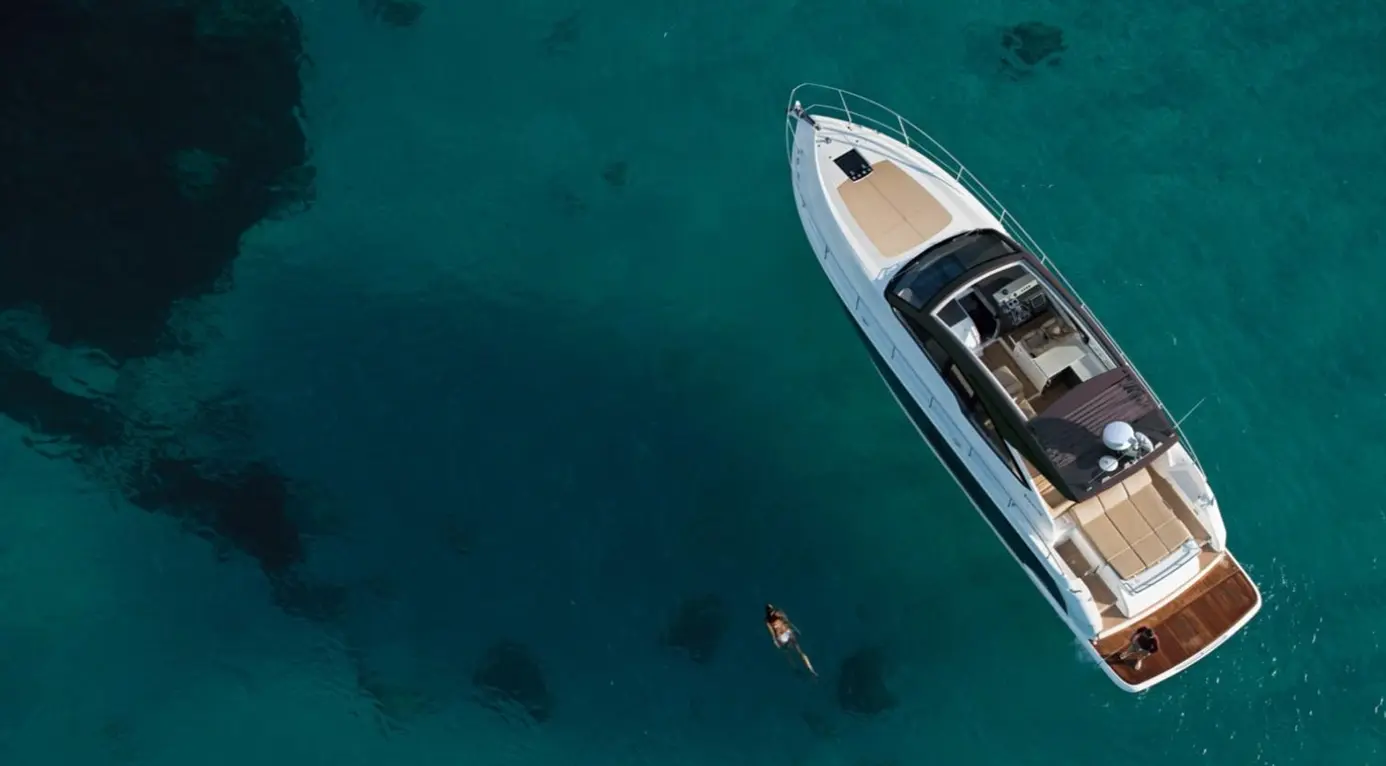 Aerial view of a luxurious yacht on clear blue waters, with a swimmer near the boat enjoying a sunny day on the sea.